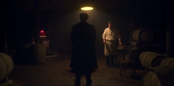 Movie still from “Peaky Blinders” (2013), created by Steven Knight – Two men standing in a dimly - lit room , one of whom is wearing an overcoat; Wide shot, Low angle