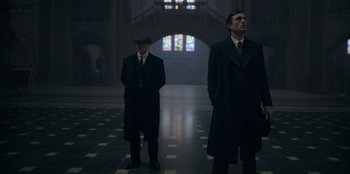 Movie still from “Peaky Blinders” (2013), created by Steven Knight – A couple of men standing next to each other in a building; Medium shot, Low angle