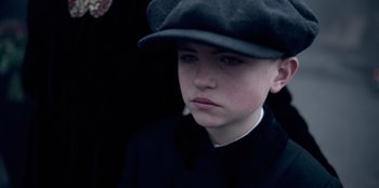 Movie still from “Peaky Blinders” (2013), created by Steven Knight – A young boy wearing a hat and a bow tie; Close Up shot, High angle