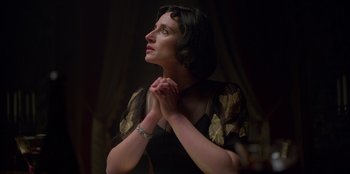Movie still from “Peaky Blinders” (2013), created by Steven Knight – A woman in a black and gold dress is praying; Close Up shot, Low angle