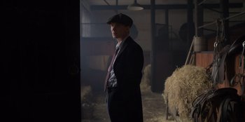 Movie still from “Peaky Blinders” (2013), created by Steven Knight – A man in a suit and tie standing in a barn; Medium shot, Low angle