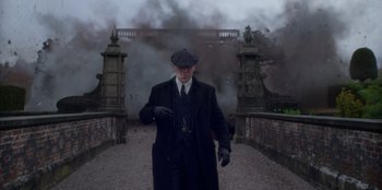 Movie still from “Peaky Blinders” (2013), created by Steven Knight – An old man in a suit and hat walking on a bridge; Medium shot, Low angle