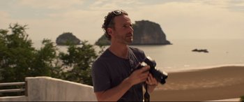Movie still from “Penguin Bloom” (2020), directed by Glendyn Ivin – A man is holding a camera while standing by the ocean; Medium shot, Over the shoulder angle