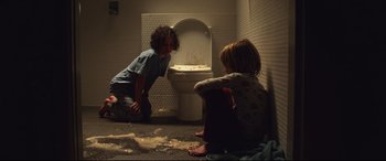 Movie still from “Penguin Bloom” (2020), directed by Glendyn Ivin – Two young children sitting on the floor in front of a urinal; Medium shot, Overhead angle