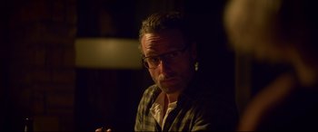 Movie still from “Penguin Bloom” (2020), directed by Glendyn Ivin – A man with glasses is sitting in a dimly - lit room; Close Up shot, Over the shoulder angle