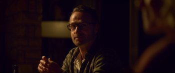 Movie still from “Penguin Bloom” (2020), directed by Glendyn Ivin – A man wearing glasses sitting in a dimly - lit room; Close Up shot, Over the shoulder angle