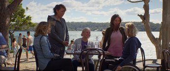 Movie still from “Penguin Bloom” (2020), directed by Glendyn Ivin – A group of people standing around a table with wine glasses; Medium shot, Over the shoulder angle