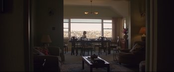 Movie still from “Penguin Bloom” (2020), directed by Glendyn Ivin – A woman sitting at a table in front of a large window; Wide shot, High angle