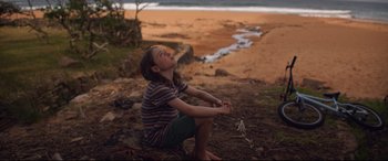 Movie still from “Penguin Bloom” (2020), directed by Glendyn Ivin – A young girl sitting on the ground near the beach; Medium shot, High angle
