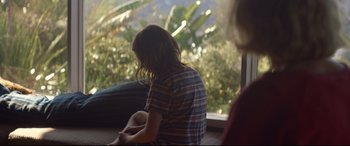 Movie still from “Penguin Bloom” (2020), directed by Glendyn Ivin – A girl sitting on a window sill looking out a window; Medium shot, Over the shoulder angle
