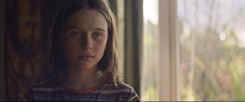 Movie still from “Penguin Bloom” (2020), directed by Glendyn Ivin – A young girl with long brown hair wearing a striped shirt looking at the camera; Close Up shot, Over the shoulder angle