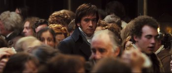 Movie still from “Pride & Prejudice” (2005), directed by Joe Wright – A man in a crowd of people looking at the camera; Medium shot, Over the shoulder angle
