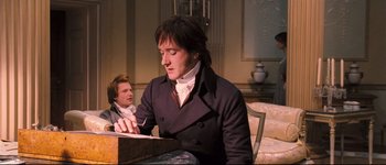 Movie still from “Pride & Prejudice” (2005), directed by Joe Wright – A man sitting in front of another man writing on a piece of paper; Medium shot, High angle