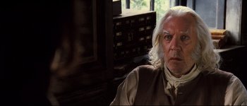 Movie still from “Pride & Prejudice” (2005), directed by Joe Wright – An older man with long white hair sitting at a desk; Close Up shot, Over the shoulder angle