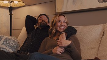 Movie still from “Prisoners” (2013), directed by Denis Villeneuve – A man and a woman sitting on a couch smiling; Medium shot, High angle