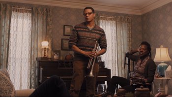 Movie still from “Prisoners” (2013), directed by Denis Villeneuve – A man standing in a living room holding a trumpet; Medium shot, Low angle