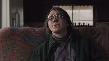 Movie still from “Prisoners” (2013), directed by Denis Villeneuve – A man sitting on a couch wearing glasses; Close Up shot, Low angle