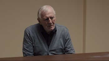 Movie still from “Prisoners” (2013), directed by Denis Villeneuve – An older man sitting at a table in front of a wall; Medium shot, Over the shoulder angle
