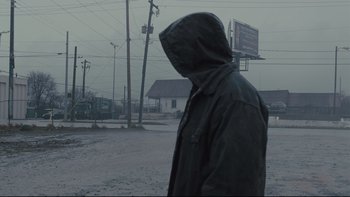 Movie still from “Prisoners” (2013), directed by Denis Villeneuve – A man in a hooded jacket walking in the rain; Wide shot, Over the shoulder angle