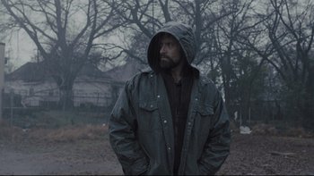 Movie still from “Prisoners” (2013), directed by Denis Villeneuve – A man in a hooded jacket standing in the rain; Medium shot, Low angle