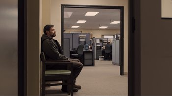 Movie still from “Prisoners” (2013), directed by Denis Villeneuve – A man sitting in a chair in a room with cubicles; Wide shot, Over the shoulder angle