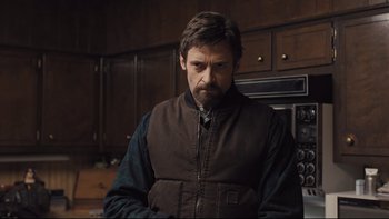 Movie still from “Prisoners” (2013), directed by Denis Villeneuve – A man standing in a kitchen wearing a vest; Medium shot, Over the shoulder angle