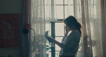 Movie still from “Private Life” (2018), directed by Tamara Jenkins – A woman standing in front of a window reading a book; Medium shot, High angle