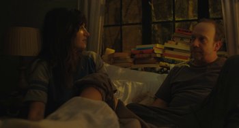 Movie still from “Private Life” (2018), directed by Tamara Jenkins – A woman sitting on a bed next to a bunch of books; Medium shot, High angle