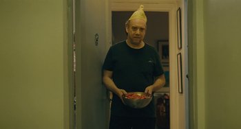 Movie still from “Private Life” (2018), directed by Tamara Jenkins – A man wearing a hat holding a bowl of food; Medium shot, Over the shoulder angle
