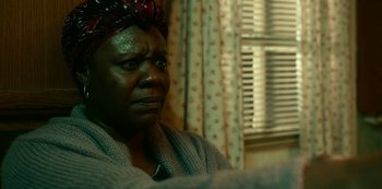 Movie still from “Project Power” (2020), directed by Henry Joost – An older woman wearing a head scarf looking out a window; Close Up shot, Over the shoulder angle