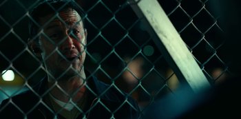 Movie still from “Project Power” (2020), directed by Henry Joost – A man looking through a chain link fence at night; Close Up shot, Over the shoulder angle