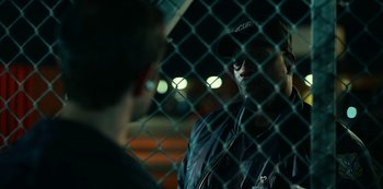 Movie still from “Project Power” (2020), directed by Henry Joost – A man wearing a baseball cap talking to another man behind a chain link fence at night; Close Up shot, Over the shoulder angle