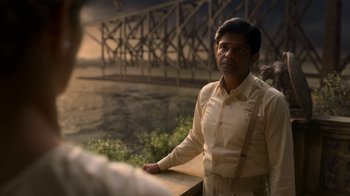 A man standing next to a river with a bridge in the background