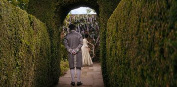 Movie still from “Queen Charlotte: A Bridgerton Story” (2023), directed by Tom Verica – A man and a woman dressed in period garb walk down a path; Wide shot, Over the shoulder angle