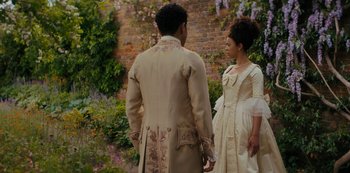 Movie still from “Queen Charlotte: A Bridgerton Story” (2023), directed by Tom Verica – A man and a woman standing next to each other in front of a brick wall; Medium shot, Over the shoulder angle