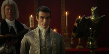 Movie still from “Queen Charlotte: A Bridgerton Story” (2023), directed by Tom Verica – A man in a suit standing in front of candles in a room; Medium shot, Over the shoulder angle