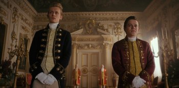Movie still from “Queen Charlotte: A Bridgerton Story” (2023), directed by Tom Verica – Two men dressed in period clothing standing in front of a door way; Medium shot, Low angle