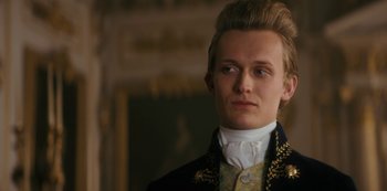 Movie still from “Queen Charlotte: A Bridgerton Story” (2023), directed by Tom Verica – A young man with blonde hair wearing a suit and tie; Close Up shot, Low angle