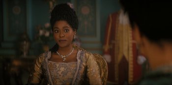 Movie still from “Queen Charlotte: A Bridgerton Story” (2023), directed by Tom Verica – A woman in a dress sitting in a chair in front of a wall; Close Up shot, Over the shoulder angle