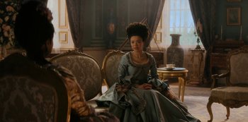 Movie still from “Queen Charlotte: A Bridgerton Story” (2023), directed by Tom Verica – A woman sitting on a chair in a room; Medium shot, Over the shoulder angle