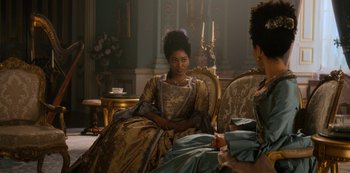 Movie still from “Queen Charlotte: A Bridgerton Story” (2023), directed by Tom Verica – Two women sitting on a chair in a room; Medium shot, Over the shoulder angle