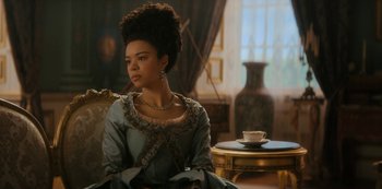 Movie still from “Queen Charlotte: A Bridgerton Story” (2023), directed by Tom Verica – A woman sitting on a chair in a living room; Medium shot, Over the shoulder angle
