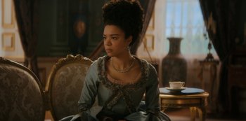 Movie still from “Queen Charlotte: A Bridgerton Story” (2023), directed by Tom Verica – A woman sitting on a chair in a room; Medium shot, Over the shoulder angle