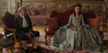Movie still from “Queen Charlotte: A Bridgerton Story” (2023), directed by Tom Verica – A man and a woman sitting on a couch in a room; Wide shot, High angle