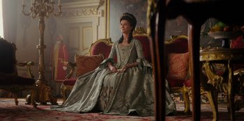 Movie still from “Queen Charlotte: A Bridgerton Story” (2023), directed by Tom Verica – A woman sitting on a couch wearing a dress; Wide shot, Low angle