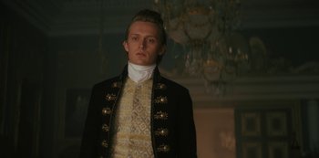 Movie still from “Queen Charlotte: A Bridgerton Story” (2023), directed by Tom Verica – A man in a black and gold suit standing in front of a chandelier; Medium shot, Low angle
