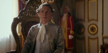 Movie still from “Queen Charlotte: A Bridgerton Story” (2023), directed by Tom Verica – An older man in a suit and wig stands in front of an older man in a suit and wig standing in front of an older man; Medium shot, Over the shoulder angle
