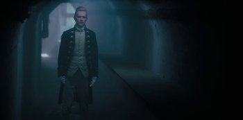 Movie still from “Queen Charlotte: A Bridgerton Story” (2023), directed by Tom Verica – A man in a suit standing in a dark room; Medium shot, Low angle
