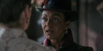 Movie still from “Queen Charlotte: A Bridgerton Story” (2023), directed by Tom Verica – An older woman wearing a red hat and a jacket; Close Up shot, Over the shoulder angle
