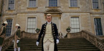 Movie still from “Queen Charlotte: A Bridgerton Story” (2023), directed by Tom Verica – A man in a suit and white gloves standing in front of a building; Medium shot, Low angle